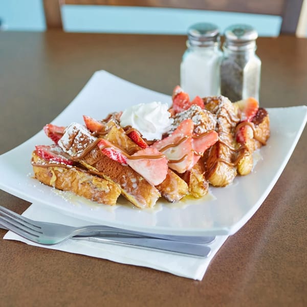 French toast with strawberries, whipped cream, and syrup on a white plate at Pacific Cafe.