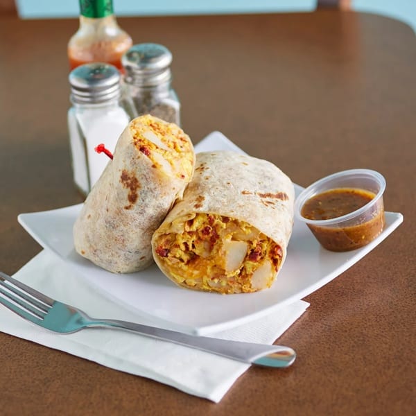 Two breakfast burritos filled with eggs and potatoes, served with salsa, salt, pepper, and hot sauce.