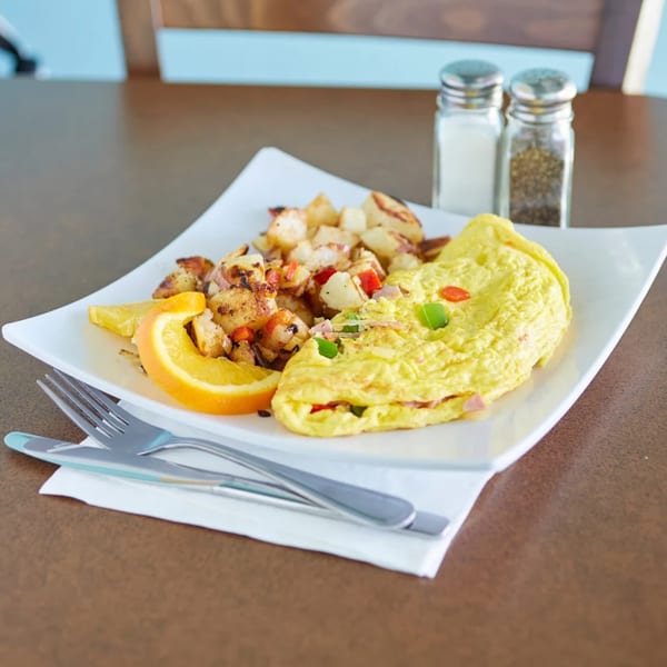 A breakfast plate with a fluffy omelet, home fries, and an orange slice, with salt and pepper shakers.