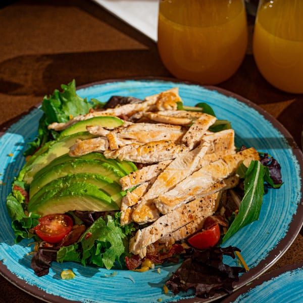 Grilled chicken and avocado salad with cherry tomatoes and mixed greens on a blue plate.