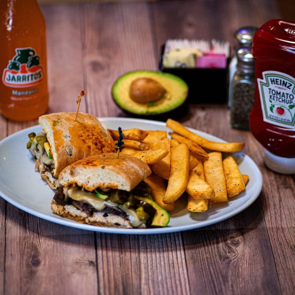 A Pacific Cafe Mexican sandwich with fries, avocado, Jarritos, and ketchup on a wooden table.
