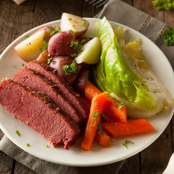 Sliced corned beef, red potatoes, carrots, and cabbage on a white plate on a wooden table.